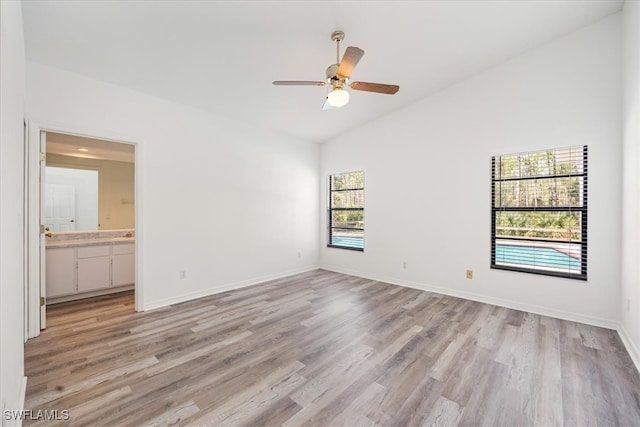 unfurnished bedroom featuring ceiling fan, vaulted ceiling, ensuite bathroom, and light wood-type flooring