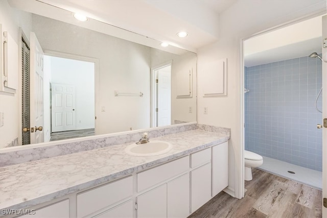 bathroom featuring toilet, hardwood / wood-style floors, vanity, and tiled shower