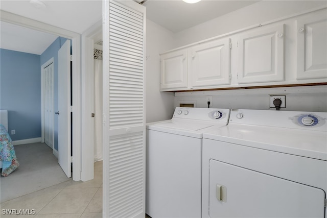 clothes washing area with cabinets, washing machine and dryer, and light tile patterned floors