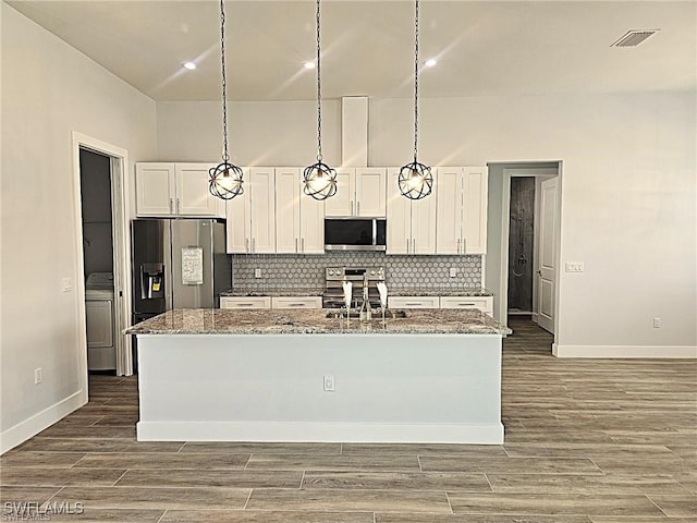 kitchen featuring appliances with stainless steel finishes, white cabinets, light stone countertops, and a center island with sink