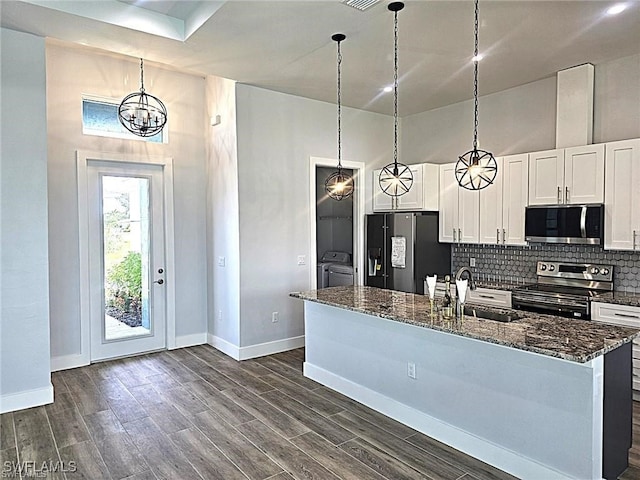 kitchen featuring stainless steel appliances, dark stone counters, sink, white cabinets, and washing machine and clothes dryer