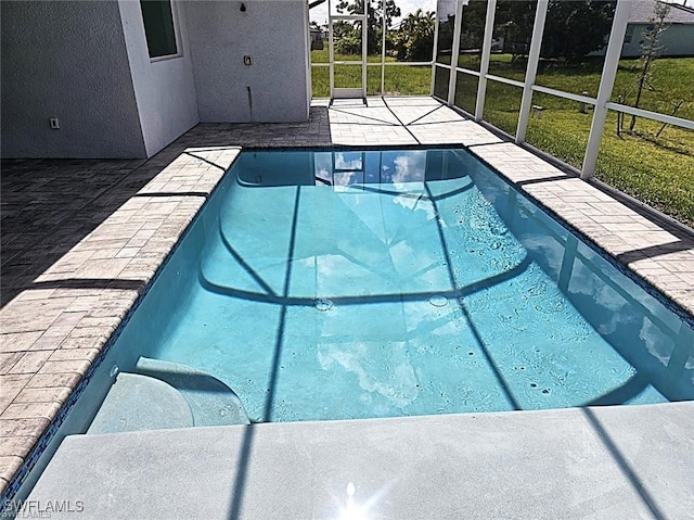 view of swimming pool featuring a yard, a patio area, and glass enclosure