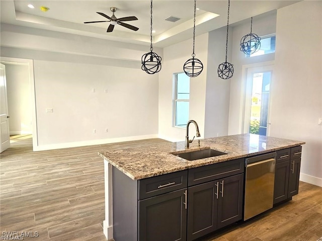 kitchen with light stone counters, stainless steel dishwasher, a tray ceiling, light hardwood / wood-style flooring, and sink