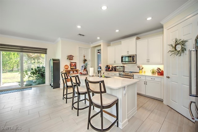 kitchen with appliances with stainless steel finishes, sink, an island with sink, a kitchen bar, and white cabinetry