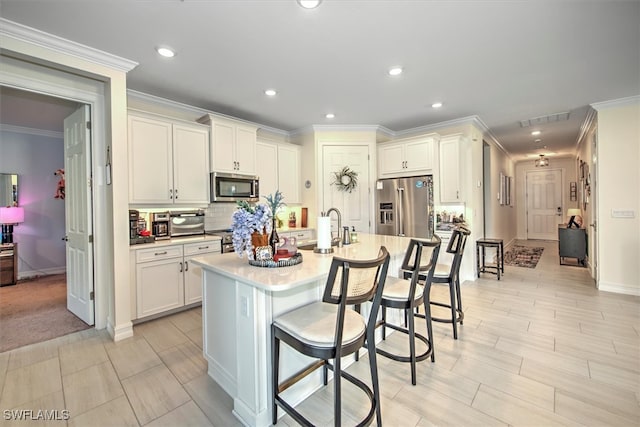 kitchen with an island with sink, sink, a breakfast bar, white cabinets, and appliances with stainless steel finishes