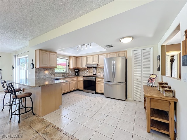 kitchen featuring backsplash, rail lighting, light stone countertops, kitchen peninsula, and stainless steel appliances