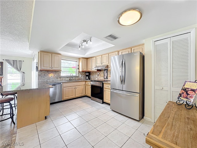 kitchen featuring a breakfast bar, stainless steel appliances, kitchen peninsula, decorative backsplash, and light brown cabinetry