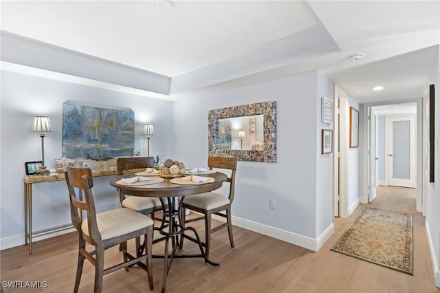 dining area with a tray ceiling, wood finished floors, and baseboards
