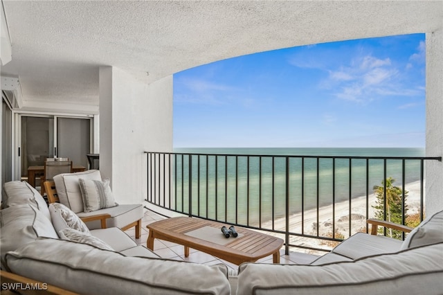 balcony with a view of the beach, an outdoor living space, and a water view