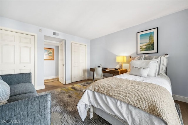 bedroom featuring baseboards, wood finished floors, visible vents, and two closets