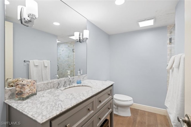 bathroom with wood finished floors, toilet, vanity, baseboards, and a stall shower