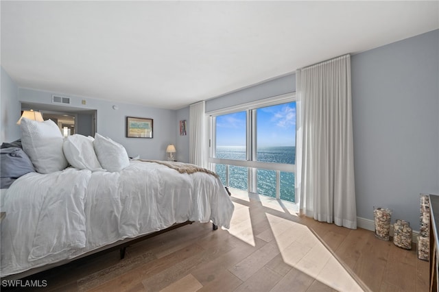 bedroom featuring wood finished floors, a water view, access to exterior, visible vents, and baseboards