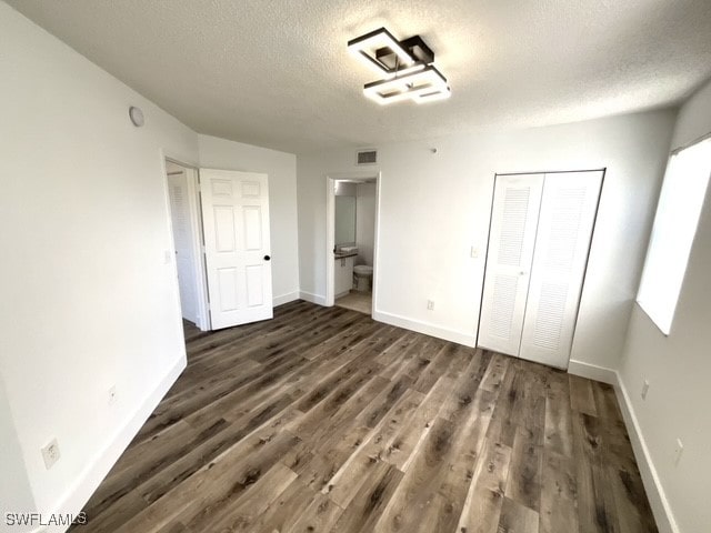 unfurnished bedroom with a closet, dark hardwood / wood-style floors, ensuite bathroom, and a textured ceiling