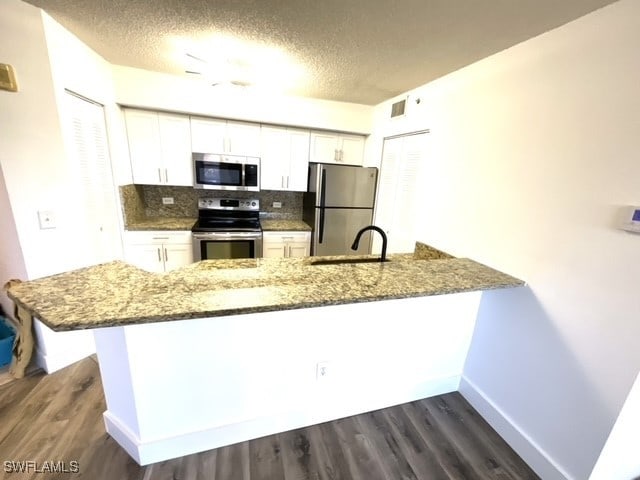 kitchen featuring appliances with stainless steel finishes, kitchen peninsula, white cabinetry, and dark stone countertops