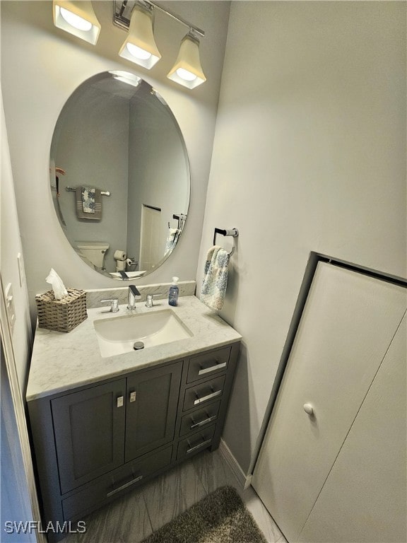 half bathroom with marble finish floor, baseboards, vanity, and toilet