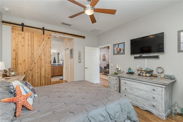 bedroom with light hardwood / wood-style flooring, a barn door, ensuite bath, and ceiling fan