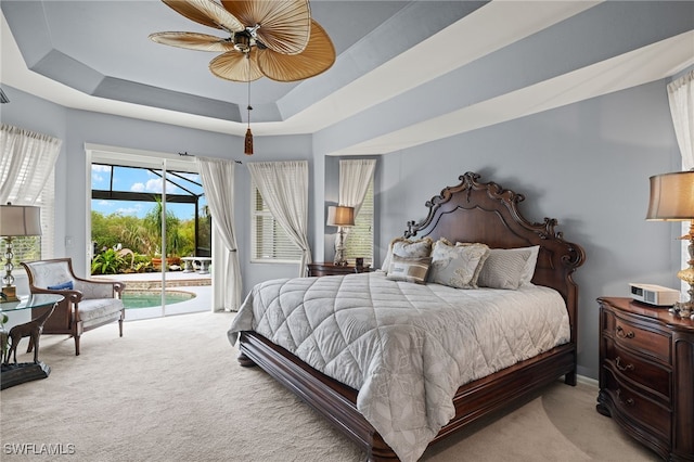 carpeted bedroom with access to exterior, a tray ceiling, and ceiling fan