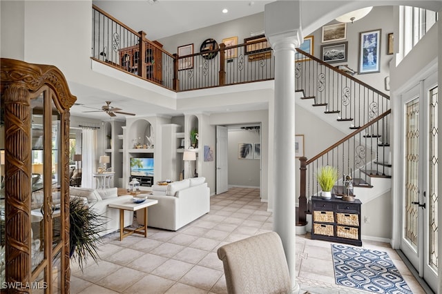 tiled living room featuring built in shelves, ceiling fan, ornate columns, a high ceiling, and french doors