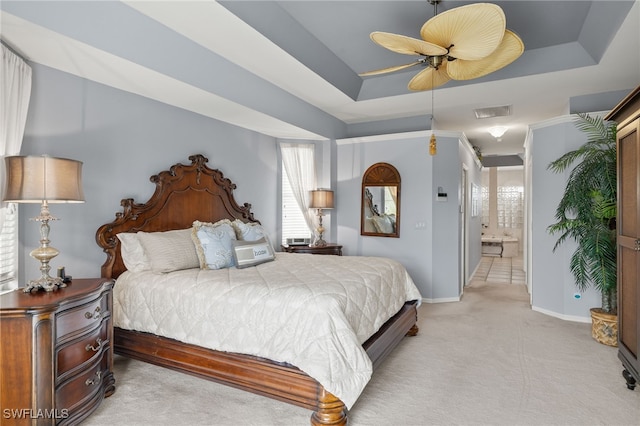 bedroom featuring light colored carpet, connected bathroom, a raised ceiling, and ceiling fan