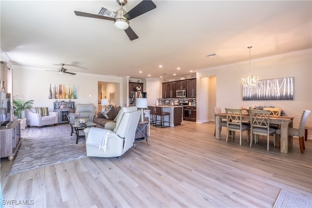 living room with light hardwood / wood-style flooring, ornamental molding, and ceiling fan with notable chandelier