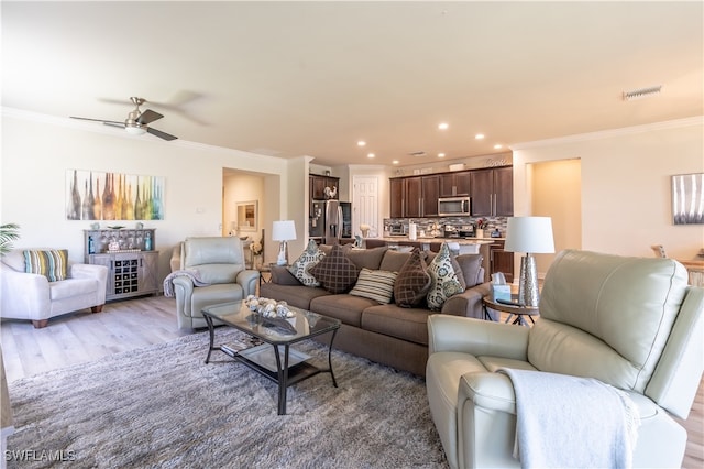 living room with ceiling fan, ornamental molding, and light wood-type flooring