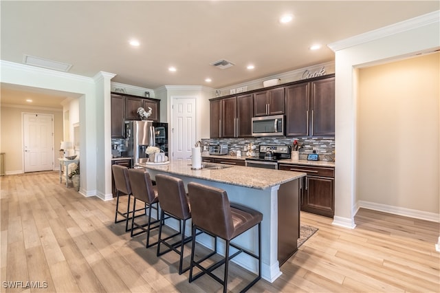 kitchen featuring appliances with stainless steel finishes, a center island with sink, backsplash, and light hardwood / wood-style floors