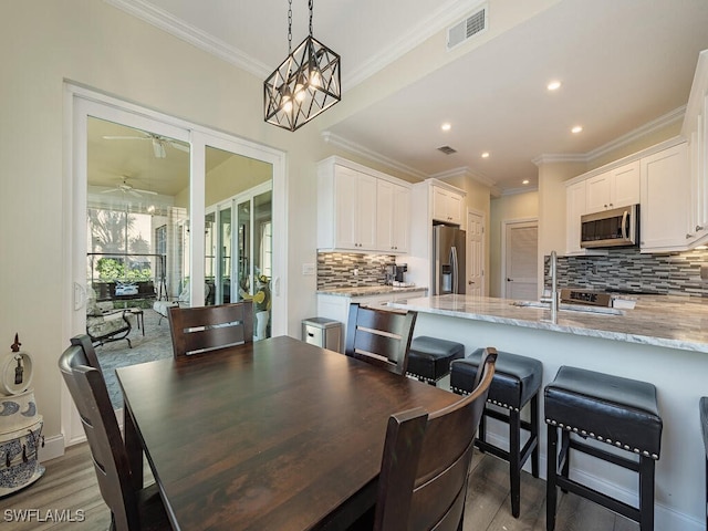 dining area with hardwood / wood-style flooring, ornamental molding, sink, and ceiling fan with notable chandelier