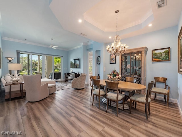 dining room with a tray ceiling, wood-type flooring, ornamental molding, and ceiling fan with notable chandelier