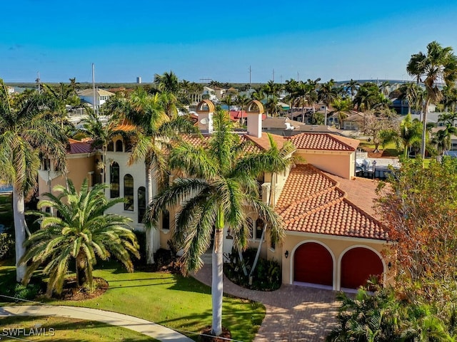 mediterranean / spanish home with an attached garage, a tile roof, a front yard, and stucco siding