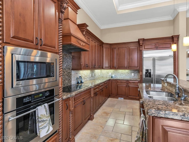 kitchen featuring premium range hood, dark stone counters, crown molding, sink, and built in appliances