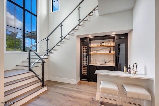 3540 Crayton Rd, Naples, FL 34103 - staircase with bar with sink, wood finished floors, baseboards, a high ceiling, and wine cooler