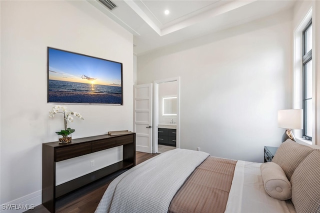 bedroom with dark hardwood / wood-style floors, a tray ceiling, and ensuite bath