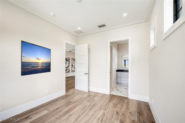 unfurnished bedroom with ensuite bathroom and light wood-type flooring