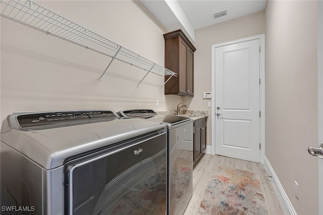 washroom featuring sink, light hardwood / wood-style flooring, washing machine and dryer, and cabinets