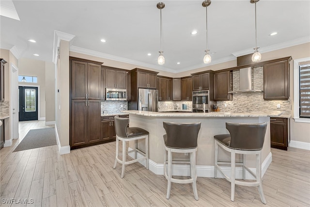 kitchen with appliances with stainless steel finishes, dark brown cabinets, hanging light fixtures, and light hardwood / wood-style floors