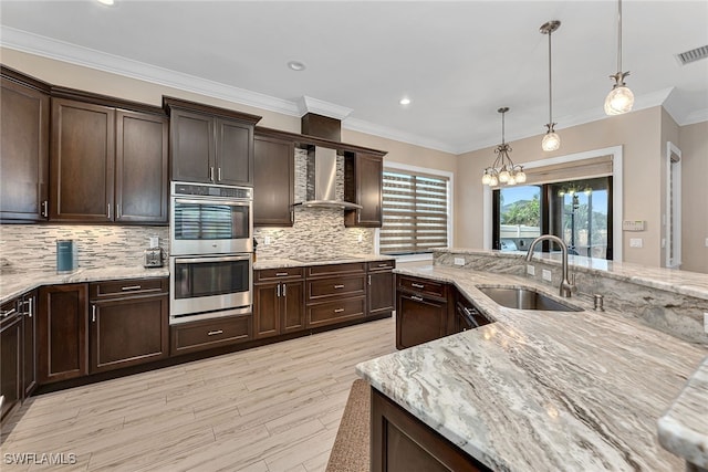 kitchen featuring double oven, hanging light fixtures, sink, light stone countertops, and dark brown cabinetry