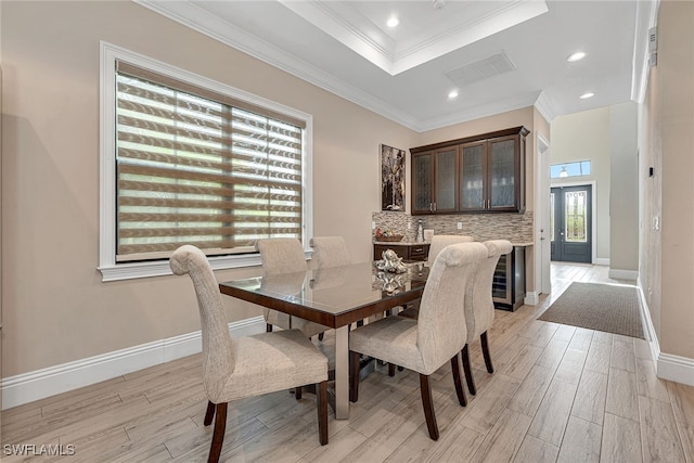 dining area featuring light hardwood / wood-style floors, crown molding, a tray ceiling, and wine cooler