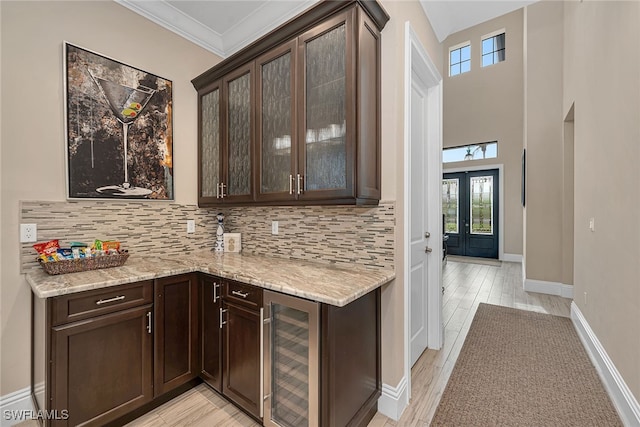 kitchen featuring decorative backsplash, light hardwood / wood-style flooring, dark brown cabinets, beverage cooler, and light stone counters