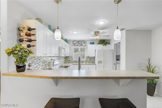 kitchen with pendant lighting, kitchen peninsula, white appliances, and a kitchen bar