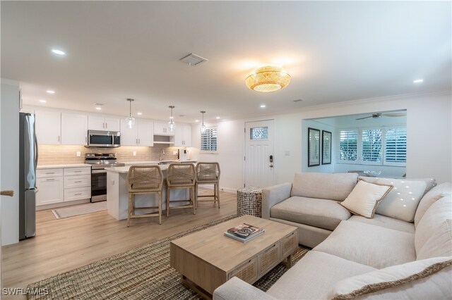 living room featuring ceiling fan, light hardwood / wood-style floors, ornamental molding, and sink