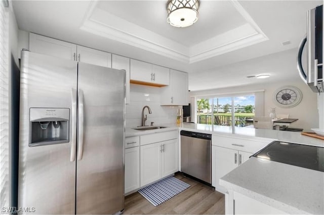 kitchen featuring stainless steel appliances, sink, a raised ceiling, white cabinets, and light wood-type flooring