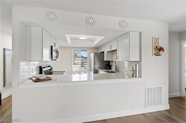 kitchen with kitchen peninsula, light hardwood / wood-style flooring, sink, white cabinetry, and appliances with stainless steel finishes