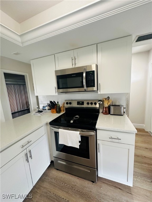 kitchen featuring white cabinets, light wood-type flooring, appliances with stainless steel finishes, and tasteful backsplash