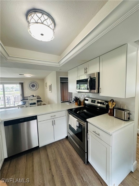 kitchen with tasteful backsplash, stainless steel appliances, white cabinets, dark wood-type flooring, and kitchen peninsula