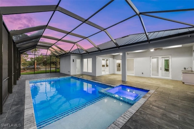 pool at dusk with glass enclosure, an in ground hot tub, a patio, and french doors