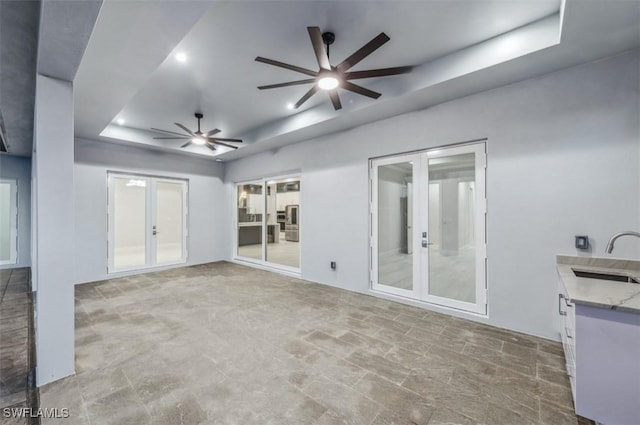 unfurnished living room featuring ceiling fan, a raised ceiling, sink, and french doors