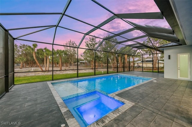 pool at dusk featuring glass enclosure, an in ground hot tub, and a patio