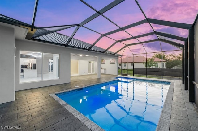 pool at dusk featuring a patio and glass enclosure