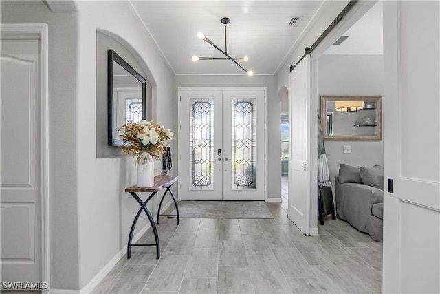 entryway with french doors, crown molding, light hardwood / wood-style flooring, a barn door, and a chandelier