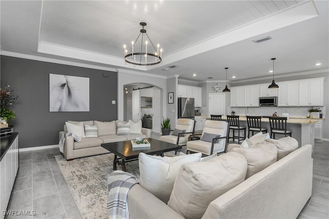 living area featuring arched walkways, visible vents, baseboards, and a tray ceiling